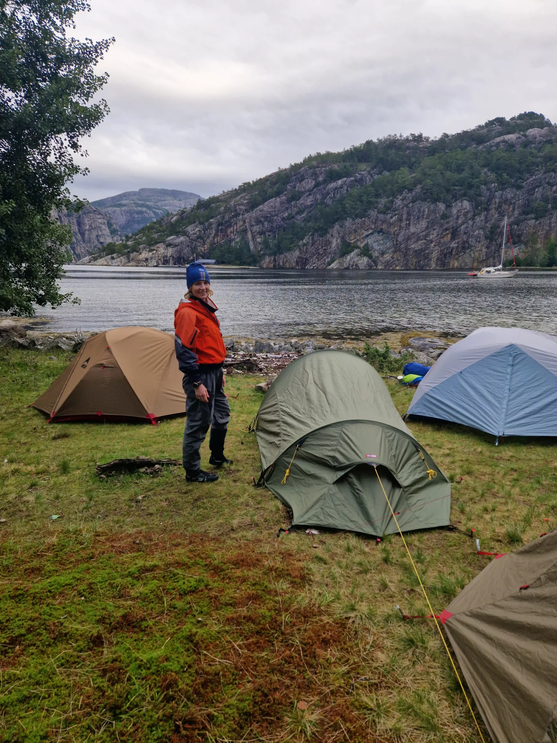 Person standing next to a pitched tent with a stunning view of the Norwegian fjords in the background