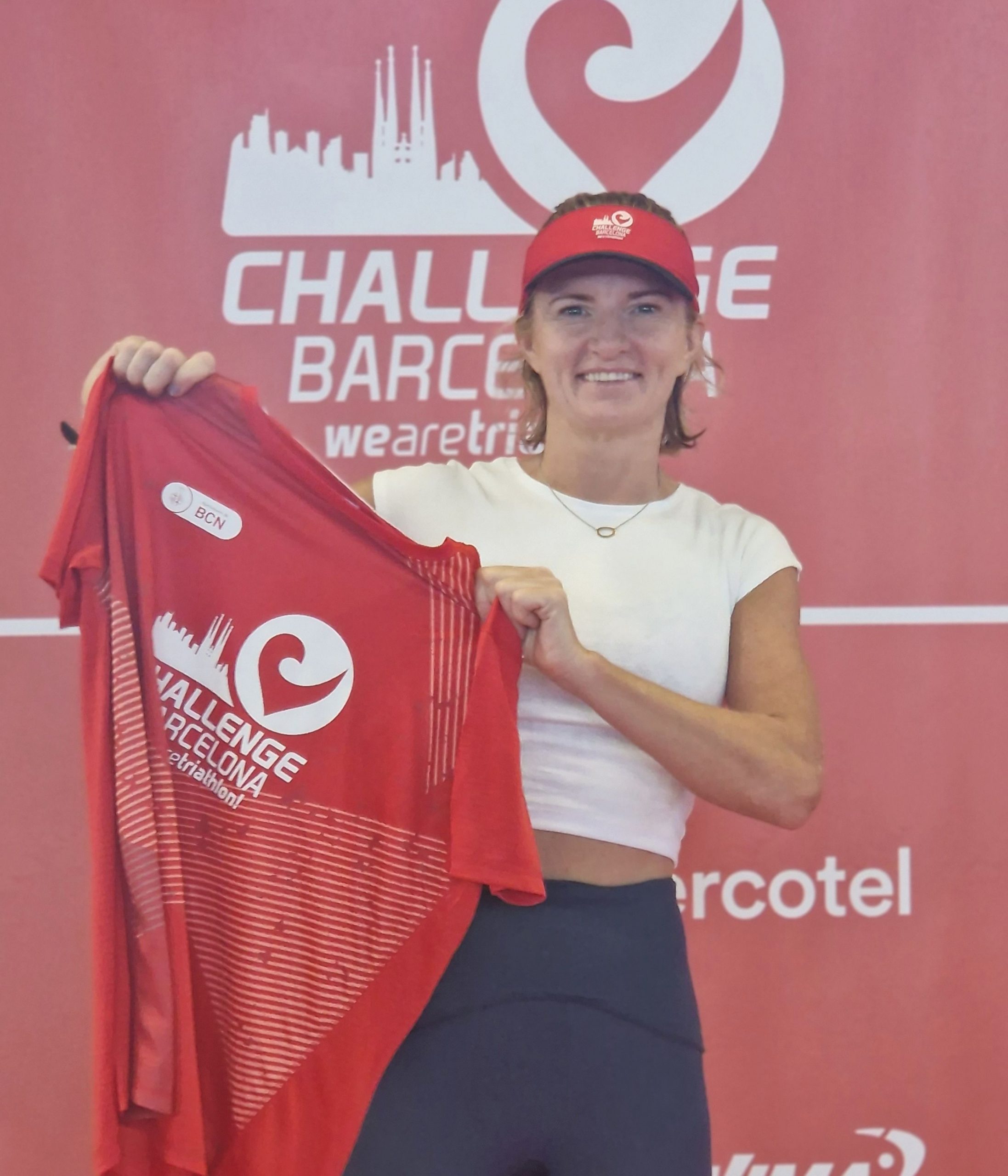 Smiling woman holding up the official Barcelona Triathlon T-shirt before registration