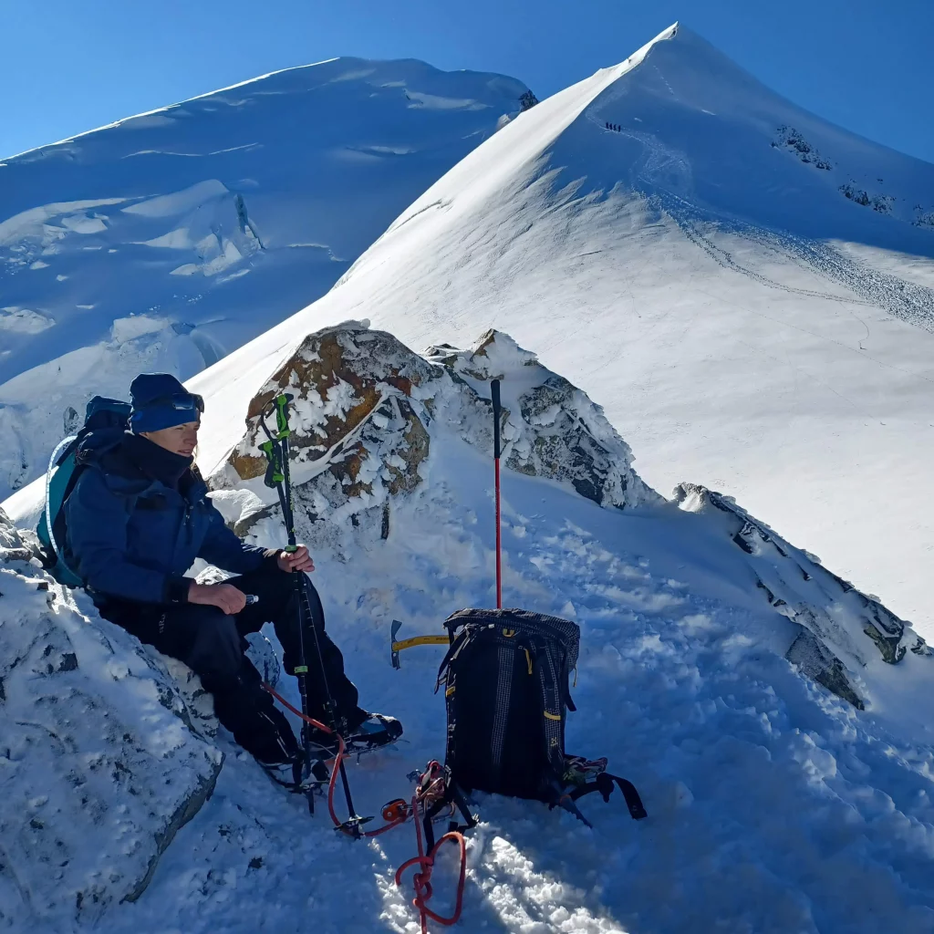 A woman sits on the snowy summit of Mont Blanc, taking a quiet moment of reflection above the clouds.