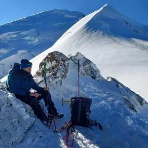 A woman sits on the snowy summit of Mont Blanc, taking a quiet moment of reflection above the clouds.