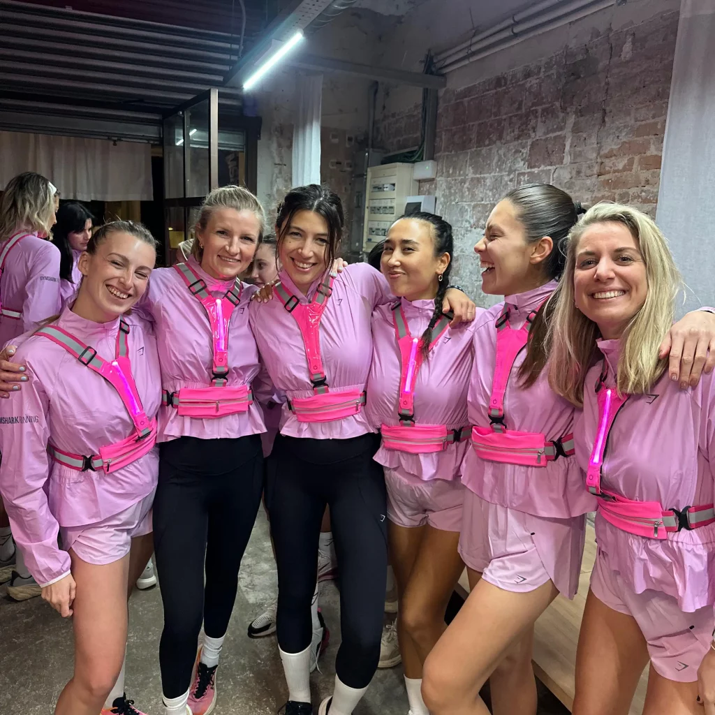 Group of female pacers in pink and high-vis gear smiling together before a nighttime 5K run in Barcelona.